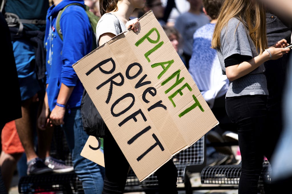 Youth climate protest with participants holding 'Planet Over Profit' sign.